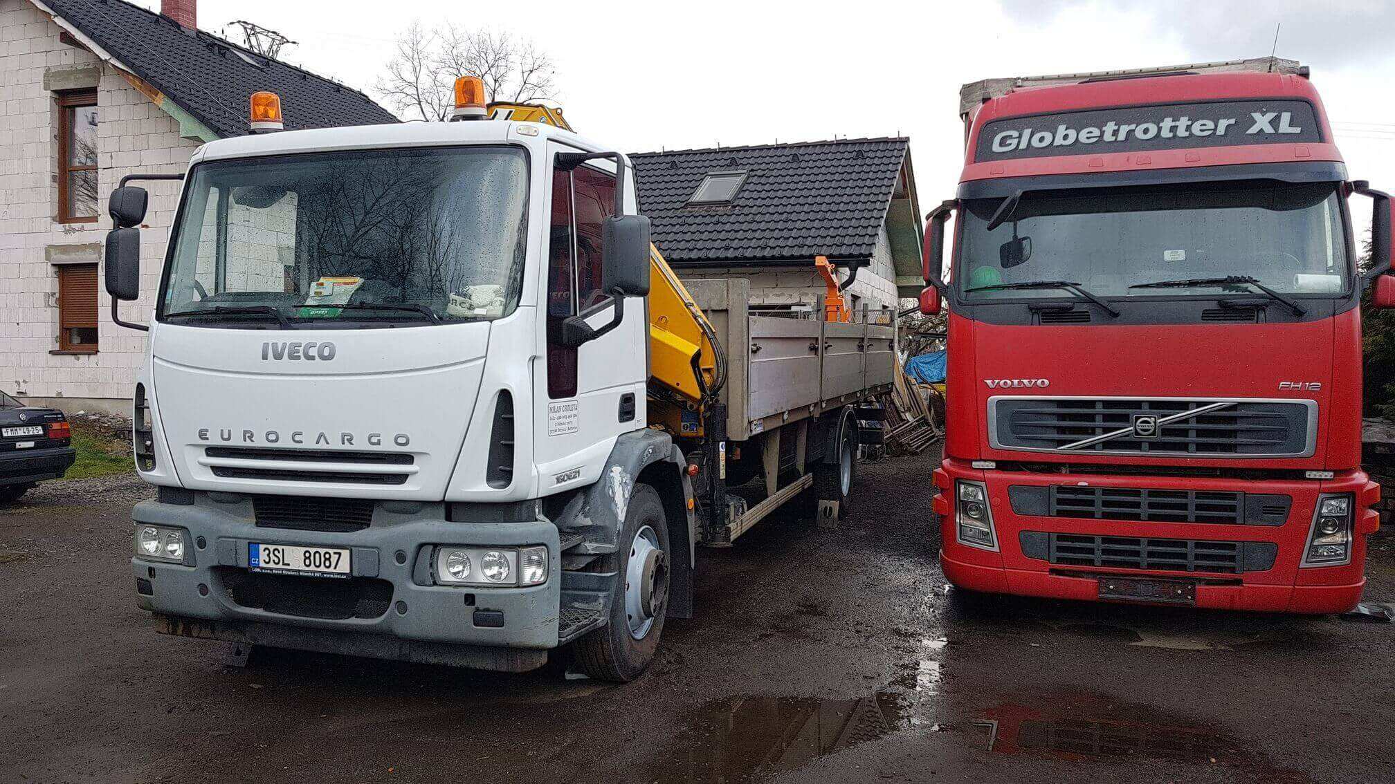 Valník Iveco EuroCargo s hydraulickou rukou vedle červeného tahače Volvo na dvoře