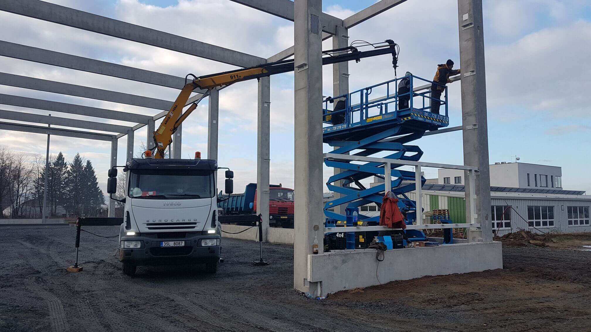Hydraulická ruka pomáhá při montáži ocelových prvků na betonovém skeletu haly