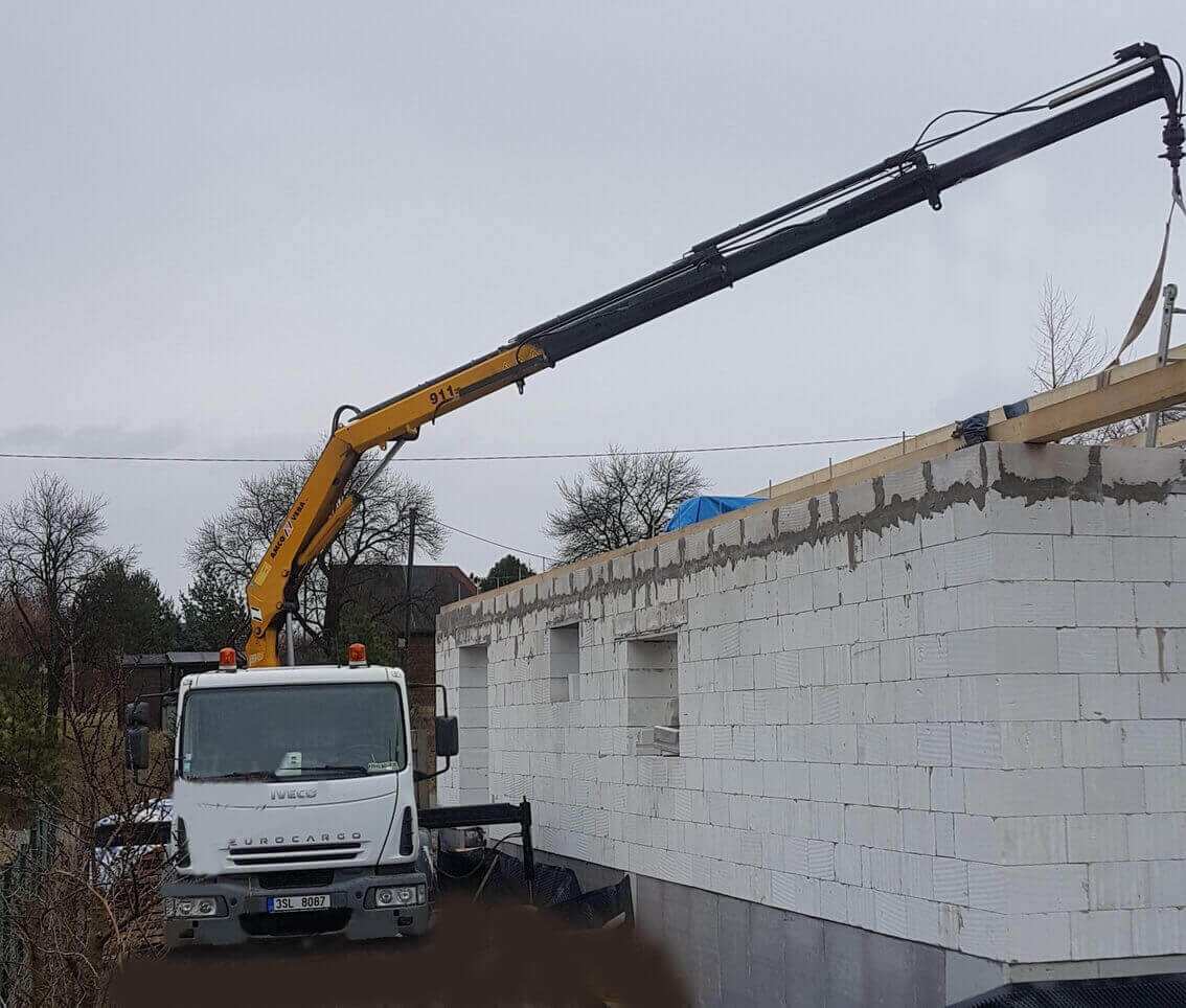 Hydraulická ruka podává materiál na hrubou stavbu rodinného domu z pórobetonu